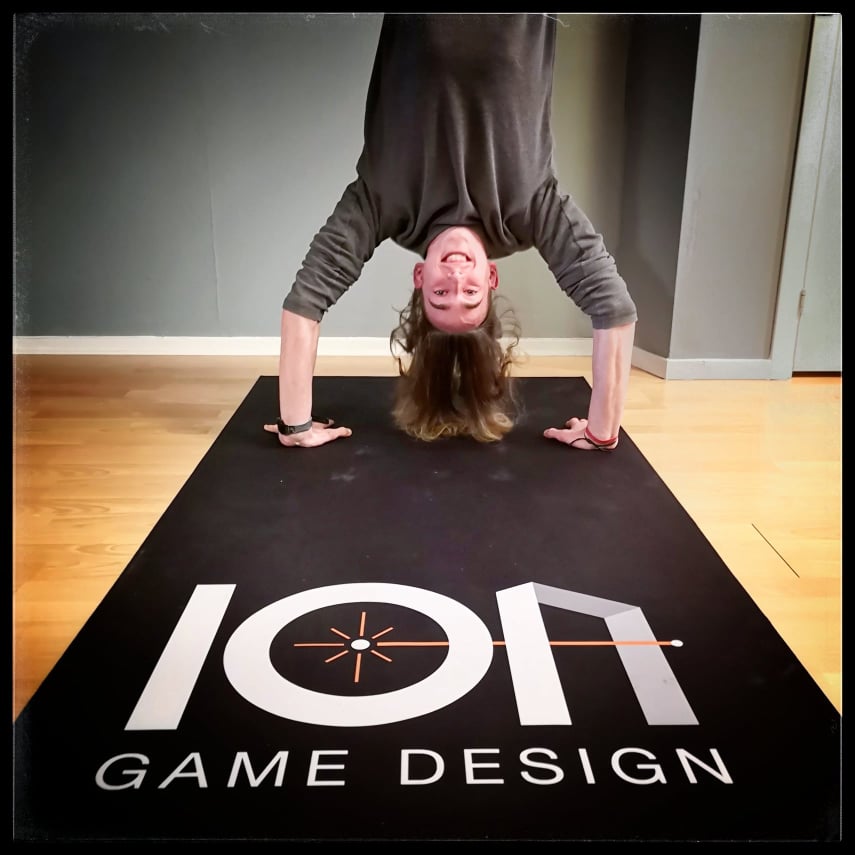 A man standing on his hands on a board game mat with company logo.