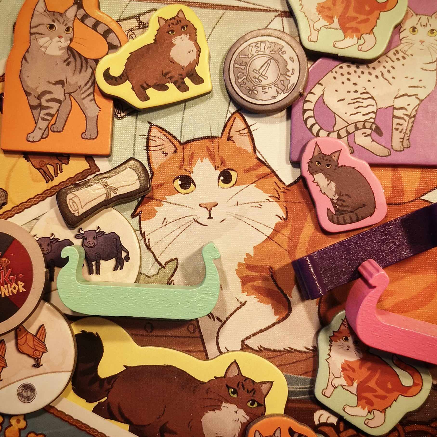 Close up of game components, like cat punch outs and wooden longships.