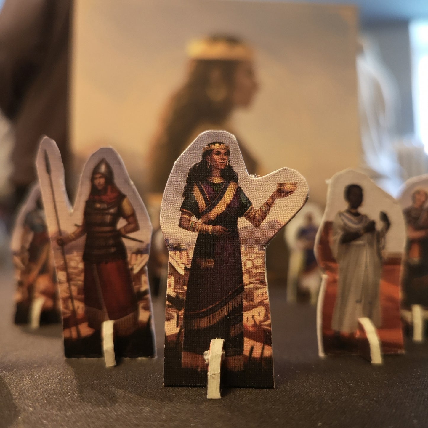 Close up of standees from the game, with queen Sammu-ramat in the center. In the background you see the game box out of focus. 