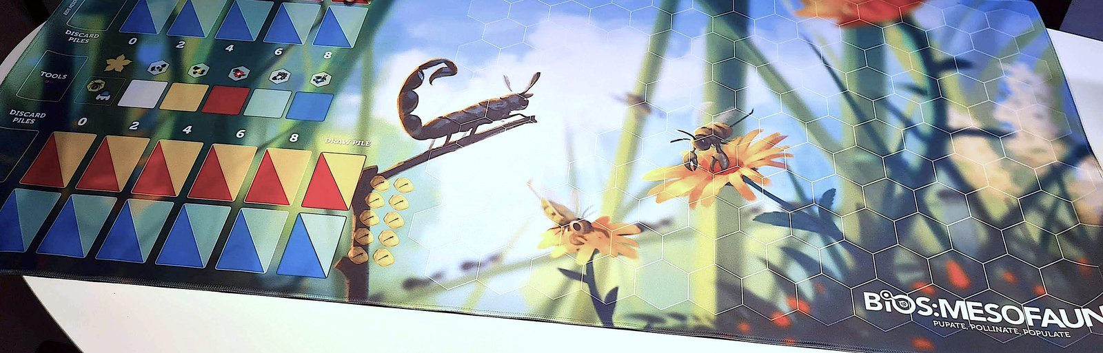 Close-up view of the game mat laid out on a table, featuring the illustrations of bugs and other plant /animal life